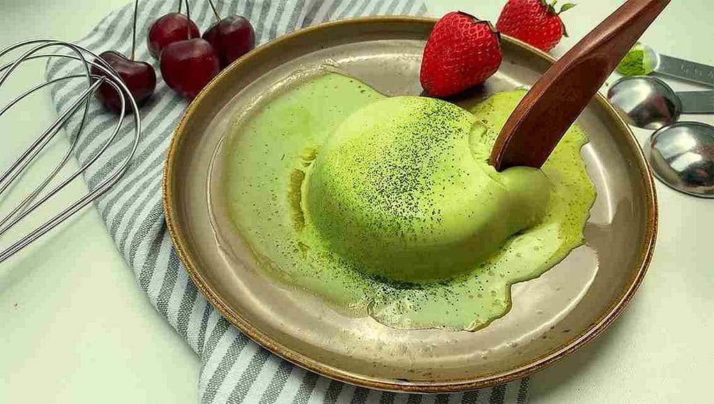 Матча-десерт с клубникой и черешней в глубокой тарелке, деревянная ложка и кухонные принадлежности на фоне